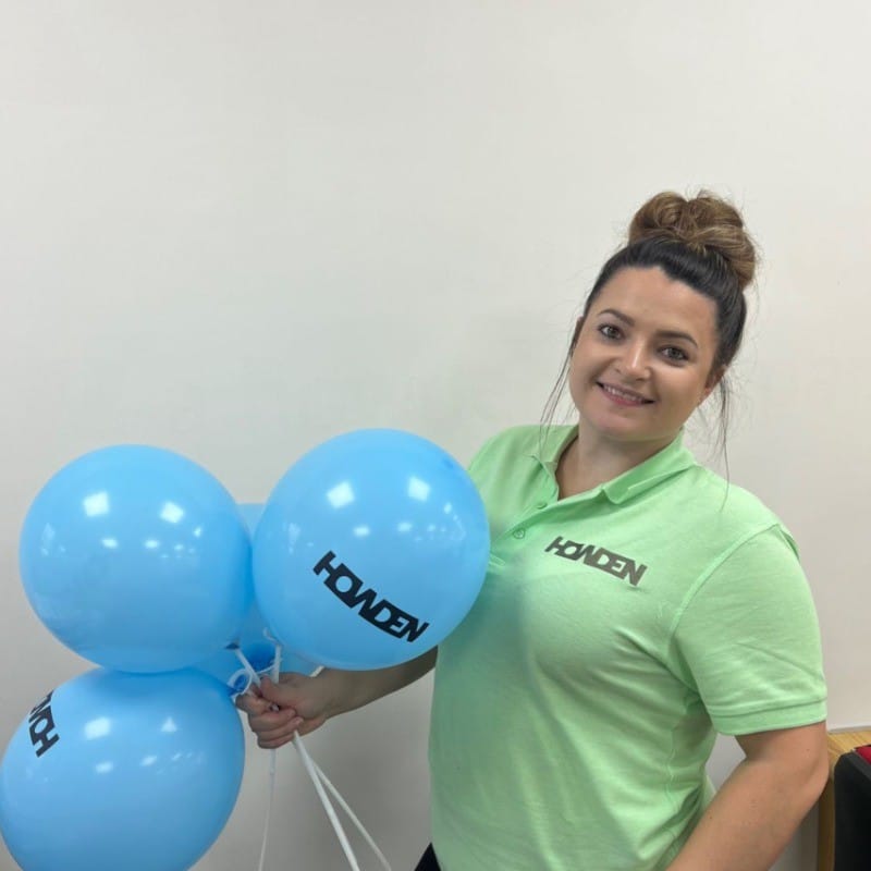 Amanda Vallance, Branch Manager at Howden Newton Abbot wearing a green Howden polo shirt and holding 3 blue Howden balloons.
