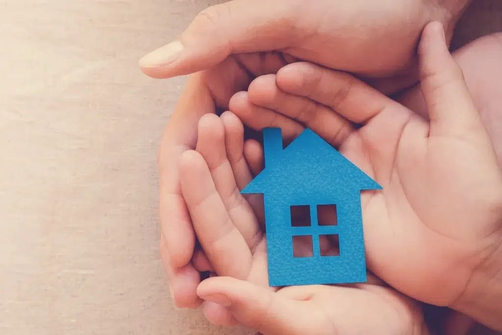 A blue cardboard house being held in a child's hands which are also being held by an adult's hands.