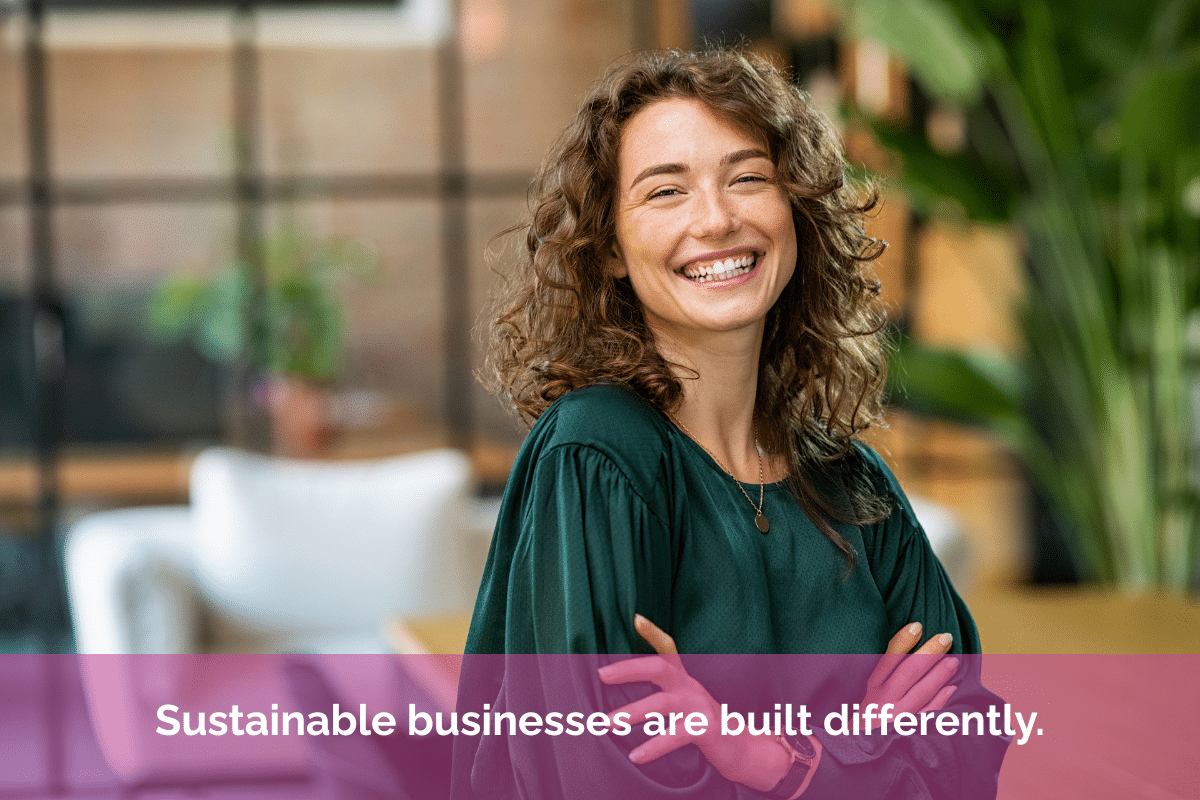 Smiling business owner standing confidently in a bright modern workspace with the quote “Sustainable businesses are built differently.” overlaid in white text on a pink banner.